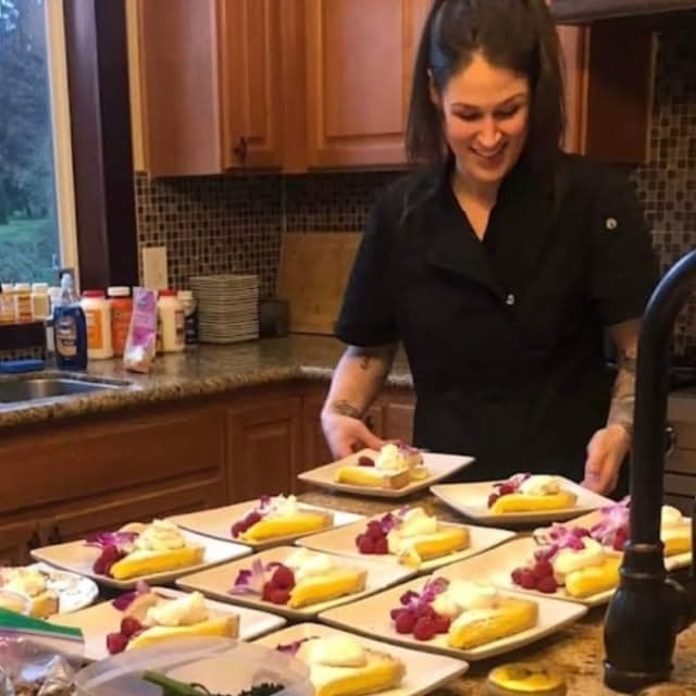 Chef Jeni in a black chef's jacket, plating individual desserts on small plates in a home kitchen.