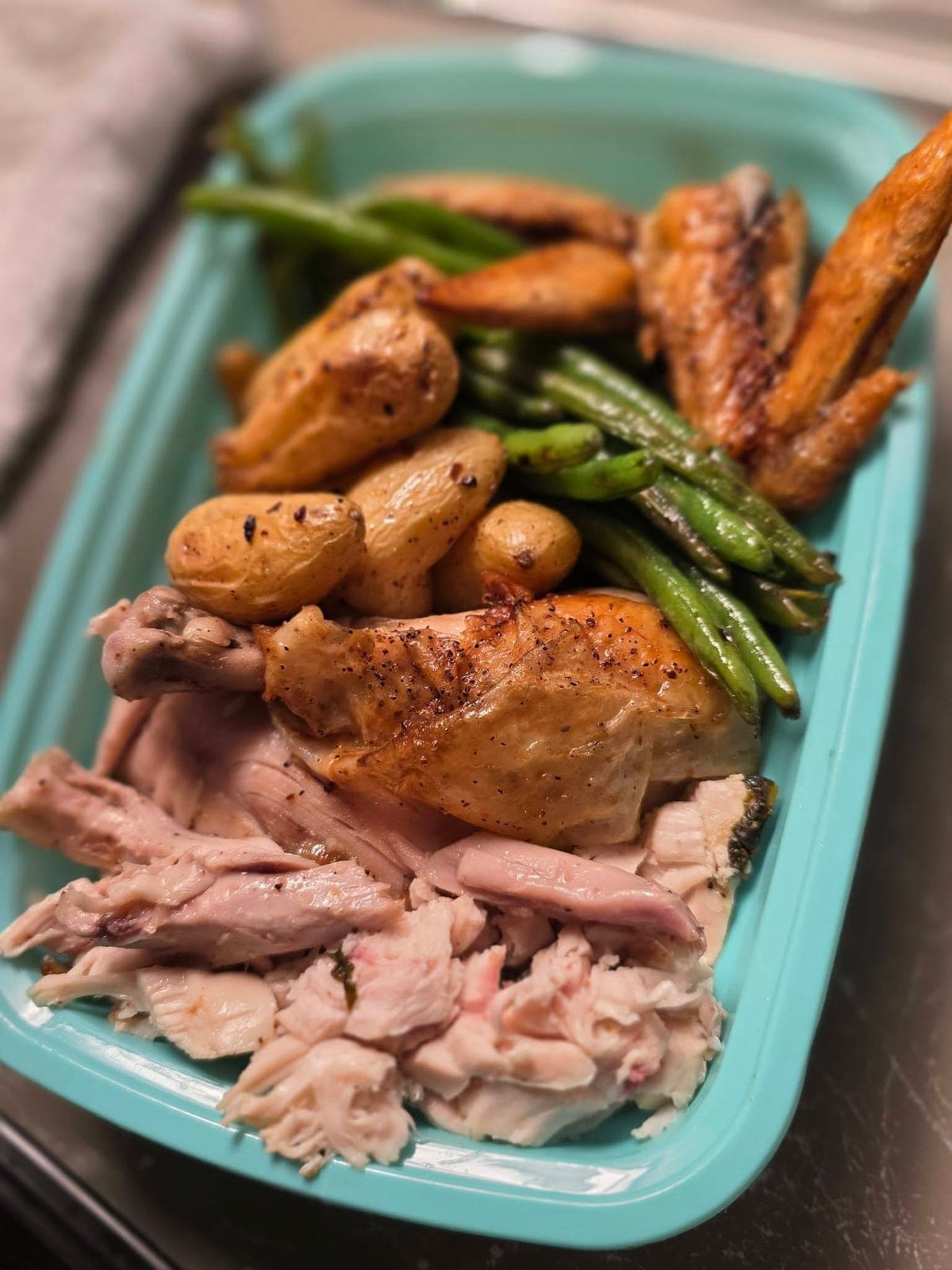 Roast chicken with fingerling potatoes and green beans in a teal dish.