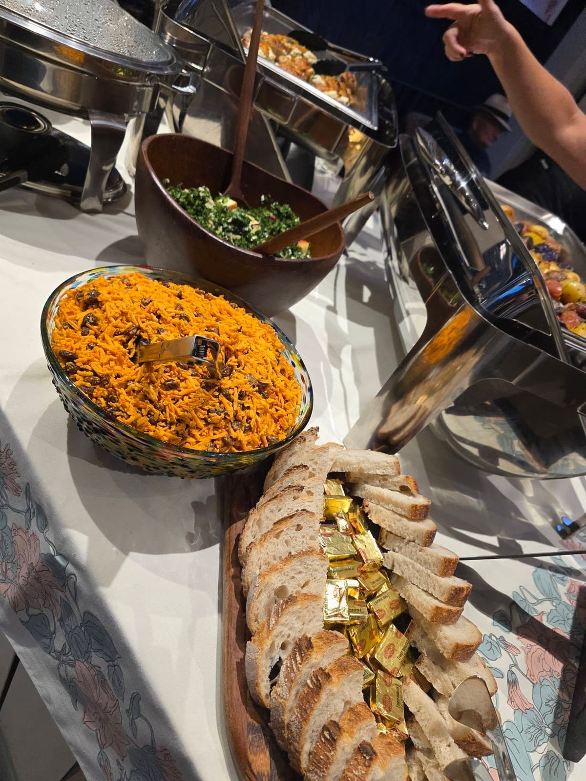 An event buffet with a carrot salad, sliced bread and chafing dishes.