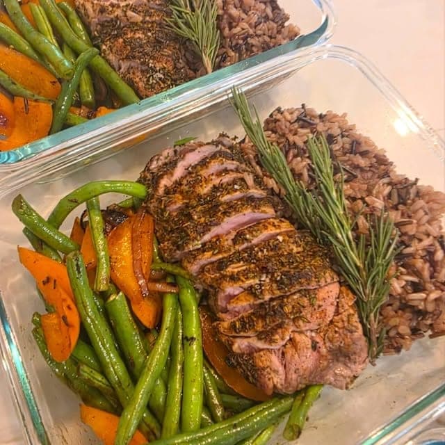 Glass meal-prep containers of herb-crusted sliced tenderloin with rosemary, wild rice, green beans and carrots.